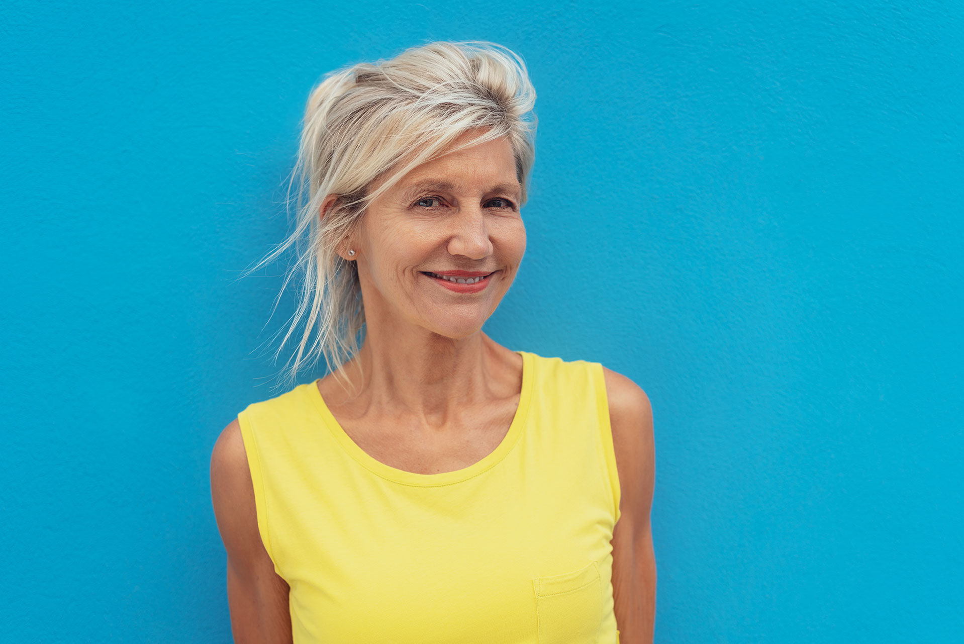 Woman in yellow shirt standing on blue wall.