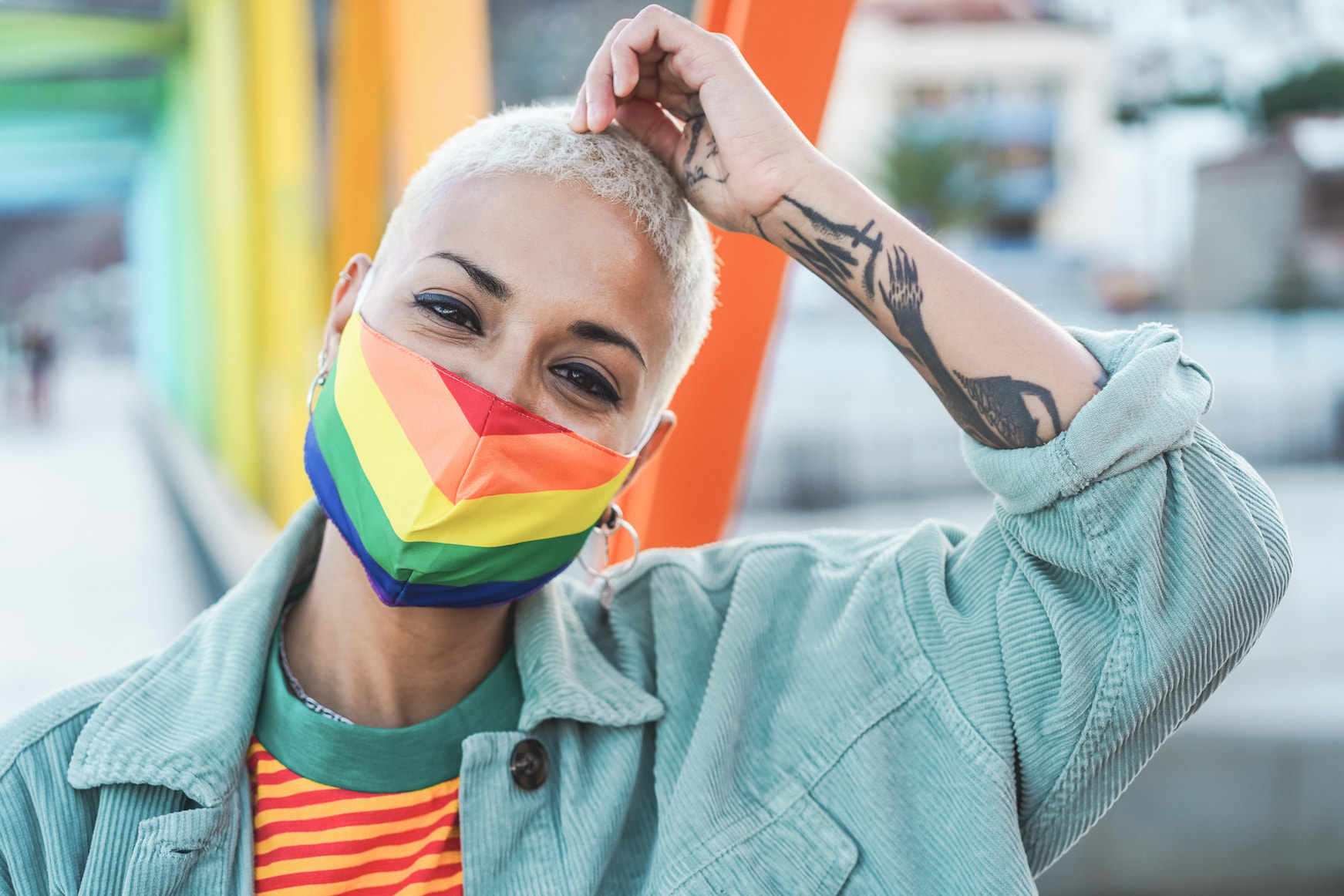 Smiling person with tattoos wearing rainbow mask